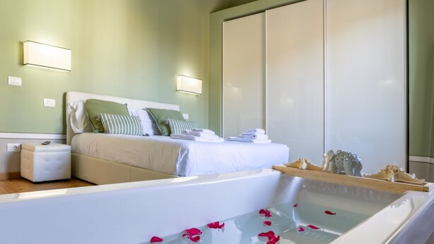 Ein modernes Schlafzimmer mit einem großen Bett, einem Nachttisch, einer eingebauten Badewanne mit Rosenblüten und einem Kleiderschrank.