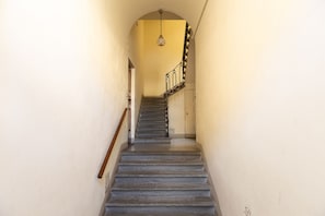 Un escalier étroit, doté d’une main courante en bois et d’une rampe noire et blanche, mène à une porte située en haut.