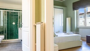 Ein Schlafzimmer mit Bett, ein Badezimmer mit Dusche und Blick auf Gebäude.
