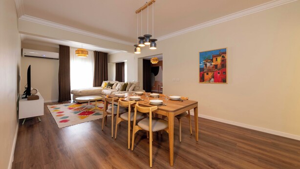 A modern dining area with a wooden table and chairs, a hanging light fixture, and a painting on the wall. - Kennah Lourina | Near Citystars, Heliopolis (Cairo)