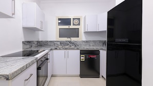 A compact kitchen with white cabinets, a black dishwasher, and a window above the sink. - Kennah Lourina | Near Citystars, Heliopolis (Cairo)