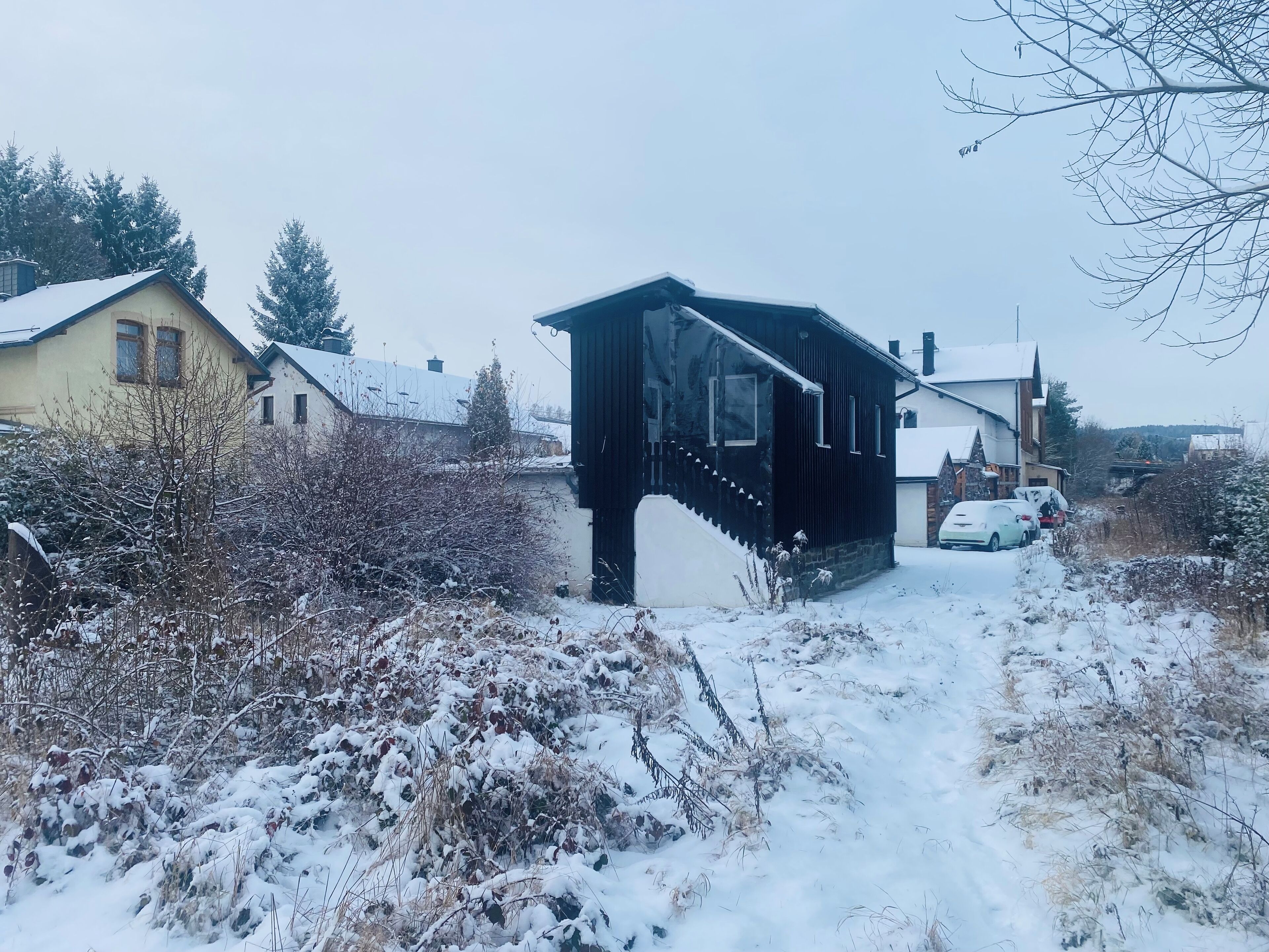 Eine kleine Holzbrücke, die zu einem Haus mit verschneitem Dach führt.