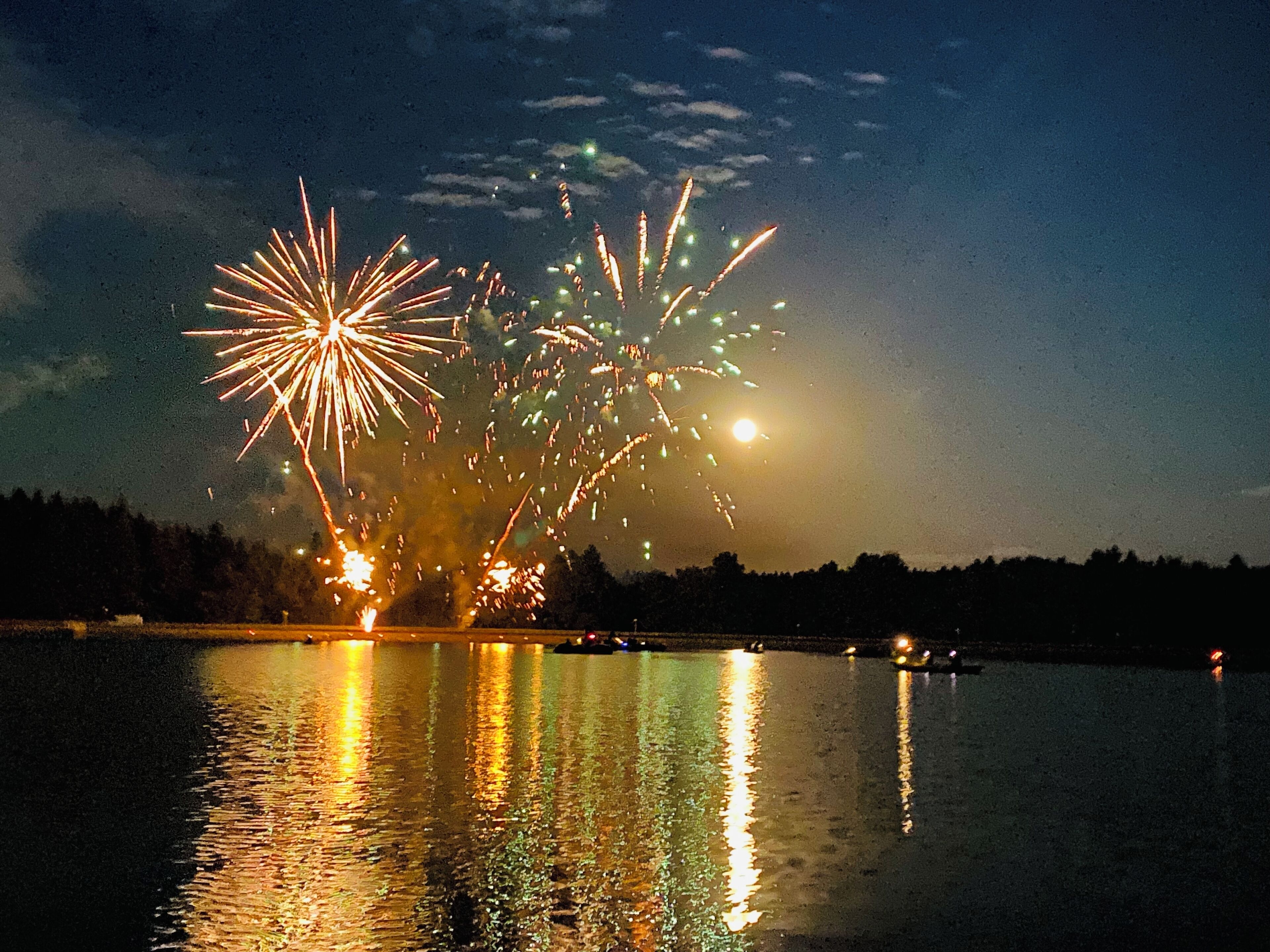 A nighttime view of fireworks over a body of water with reflections on the surface.