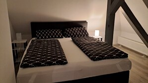 A bed with a geometric patterned bedspread, a bedside table with a lamp, and a view of the attic space.