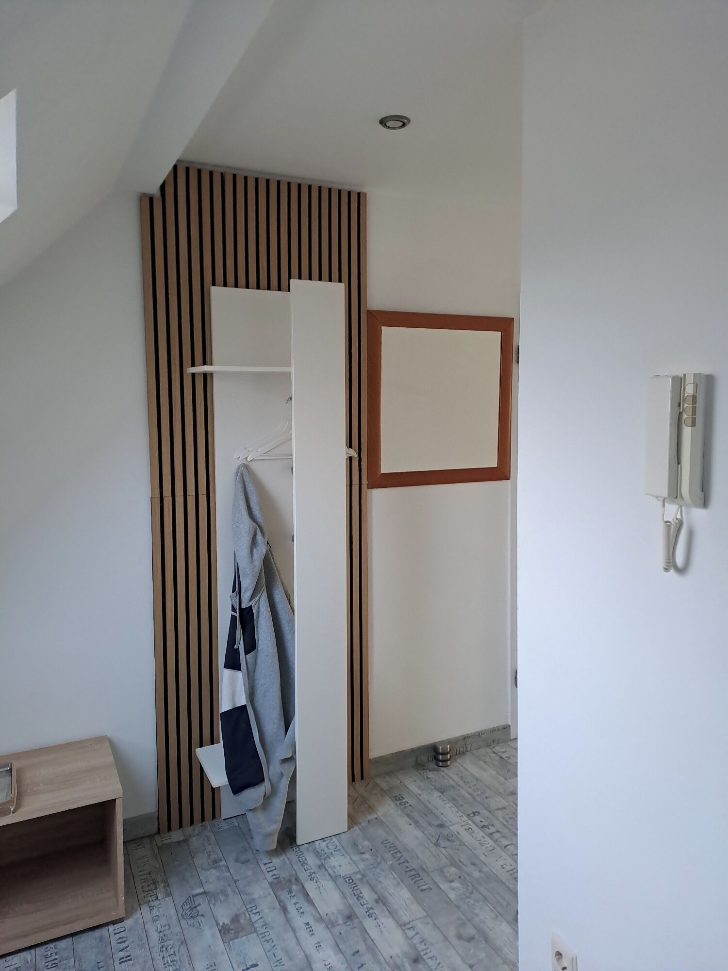 Een kamer met een wand van houten latten, een witte kast, een houten bankje en een telefoon aan de muur.
