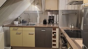 A compact kitchen with a built-in dishwasher, a coffee maker, and a stainless steel refrigerator.