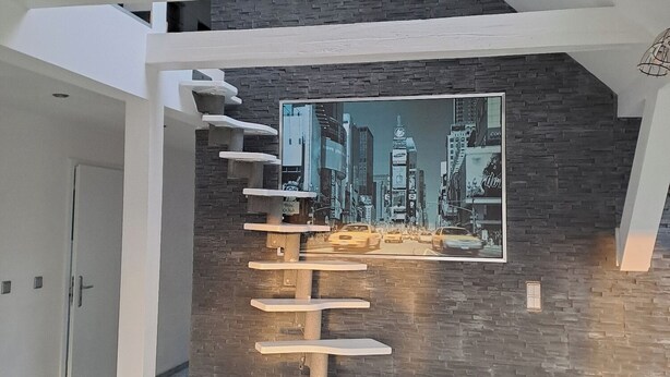 A modern interior with a staircase leading to an upper level, a cityscape mural on the wall, and a desk with a lamp.