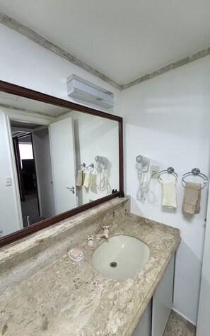 Un baño con lavamanos de mármol, un espejo grande y dos secadores de pelo fijados a la pared.