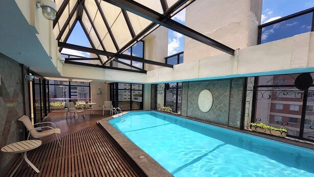 Una piscina interior con cubierta de madera, sillas de descanso y techo de vidrio.