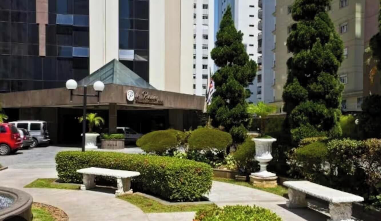 Entrada de hotel con diseño moderno, zona de estacionamiento y jardines bien cuidados.