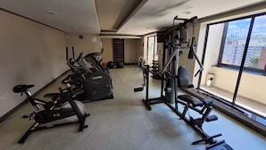 Un gimnasio con máquinas de cardio, equipo de levantamiento de pesas y un amplio ventanal con vista a la ciudad.