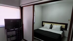 Un dormitorio con cama, televisor y puerta corredera que da a otra habitación.