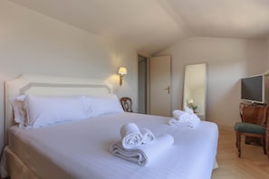 Ett hotellrum med en stor säng, två kuddar, en sänglampa, en stol, en tv och en spegel.