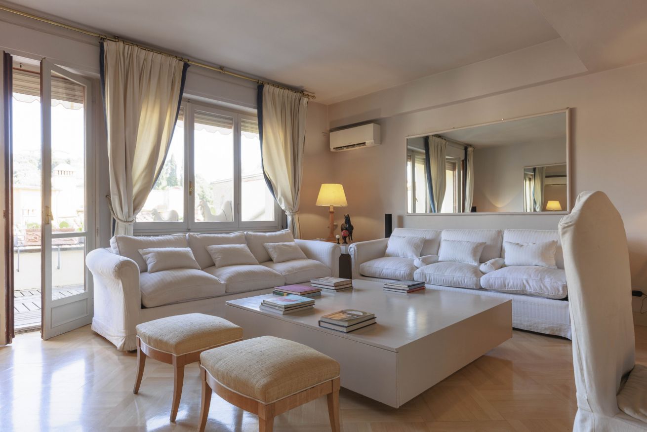 Un salón amplio con un sofá blanco grande, una mesa de centro con libros y un espejo grande.
