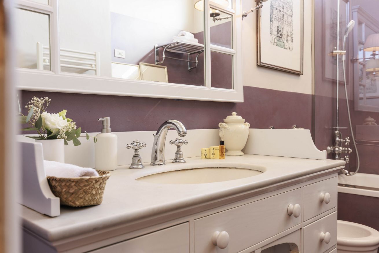 A bathroom with a double sink, a large mirror, a framed picture on the wall, and a shower area.