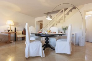 A dining area with a round table, two chairs, a lamp, and a staircase in the background.