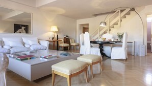 A modern living room with a sofa, ottomans, a coffee table with books, a dining table with chairs, a staircase, and a large mirror. - Pitti Secret Rooftop (Firenze)