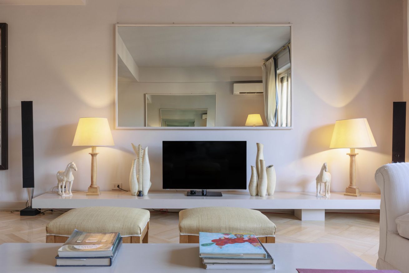 A modern living room with a flat-screen TV, two lamps, a large mirror, and a sofa.