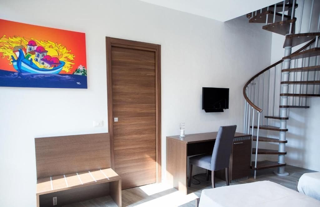 Una camera moderna con una scrivania in legno, una sedia, un letto, una porta in legno e una scala a chiocciola.