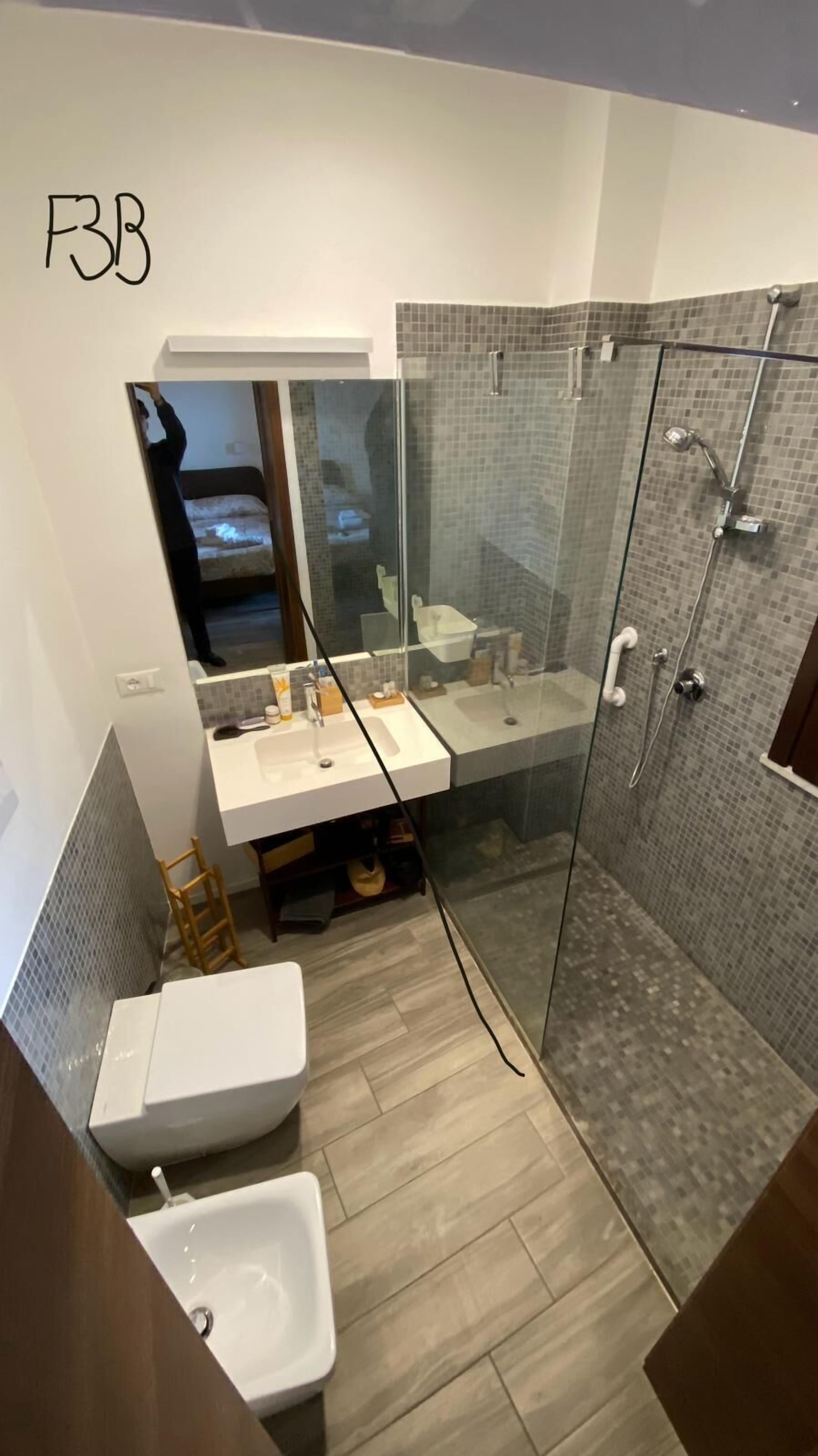 A modern bathroom with a glass shower enclosure, a double sink vanity, and a toilet.