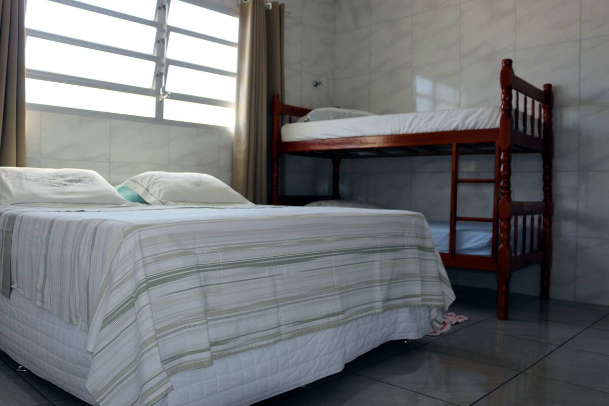 Un lit simple avec une couvre-lit à rayures, un lit superposé en bois et une fenêtre avec des rideaux.