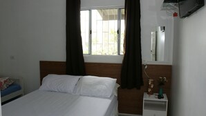 A bedroom with a bed, a nightstand, a mirror, and a window with curtains. - POUSADA DECARLI (Florianopolis)