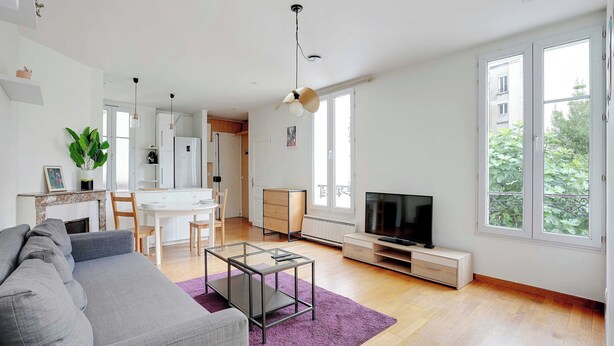 Un salon moderne avec un canapé gris, une table basse en verre, un téléviseur à écran plat et une grande fenêtre donnant sur un paysage verdoyant.