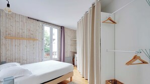 Une chambre moderne avec un mur en bois, un lit recouvert de draps blancs, un luminaire suspendu et une fenêtre avec des rideaux.