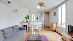 Un salon moderne avec un canapé gris, une table basse en verre et un coin repas comprenant une table et des chaises blanches.