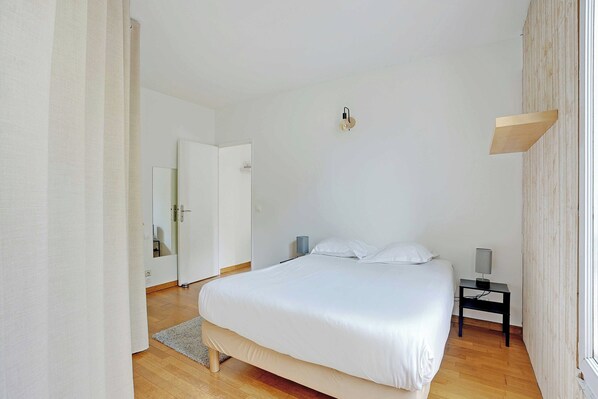 Un dormitorio con cama, mesita de noche, lámpara y espejo.