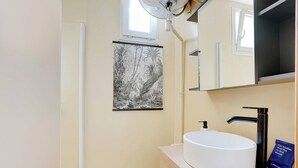 Une salle de bain avec un lavabo blanc, un robinet noir et un tabouret en bois.