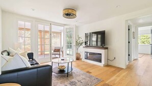 A spacious living room with a black leather sofa, a round glass coffee table, and a fireplace.