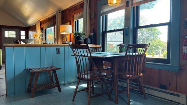 Una cocina con armarios de madera, una mesa de comedor con sillas y ventanas amplias con cortinas.