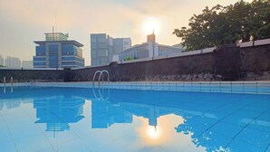 Une piscine à l’eau d’un bleu cristallin, entourée d’un mur de pierre et bordée de bâtiments modernes en arrière-plan.