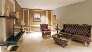 Un salon avec un canapé, un fauteuil et une table basse. Il y a un tableau au mur et une lampe sur une table d’appoint.