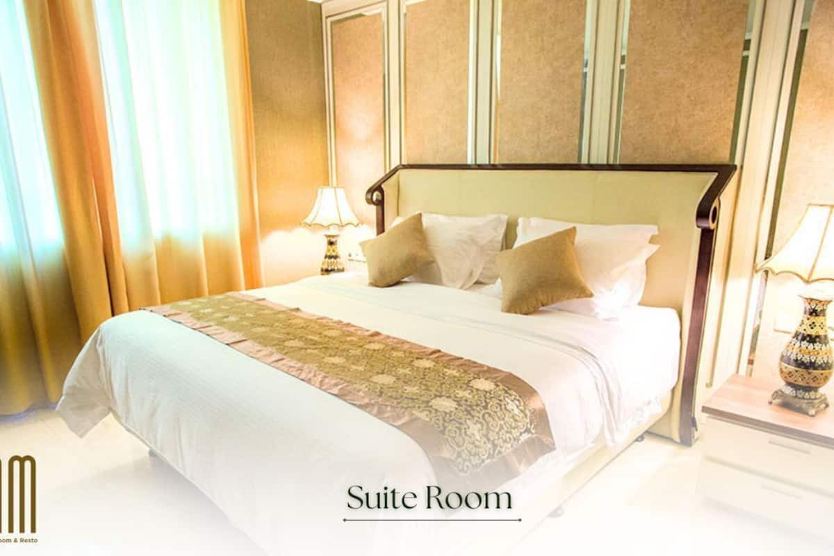 A suite room with a large bed, two bedside tables with lamps, and a view of curtains.