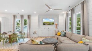 A modern living room with a sofa, ottoman, and dining area with chairs and a table. - Modern, Luxury Beach House with Private Pool and Hot Tub - Sleeps 12 (Oak Island)