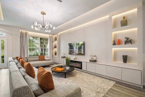 Uma sala de estar moderna com um sofá modular, uma televisão de tela plana, lareira e estantes embutidas com objetos decorativos.