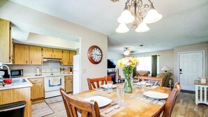 A dining area with a wooden table set for four, surrounded by wooden chairs. A clock and a vase with flowers are on the wall. - Explore Weeki Wachee Springs: Pet-friendly Home (Brooksville)