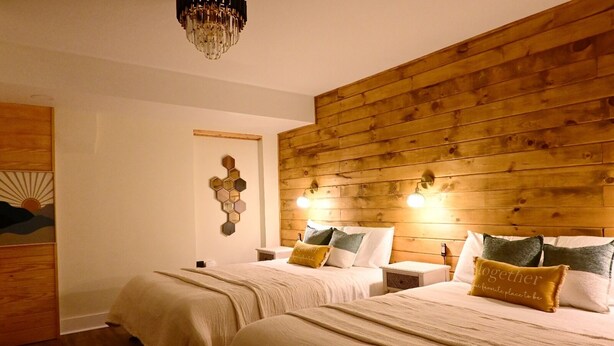 A bedroom with two beds, wooden paneling on the walls, a chandelier, and a wall-mounted light fixture. - The Aviator: Serene Ambience & Stylish Comfort (Madison)