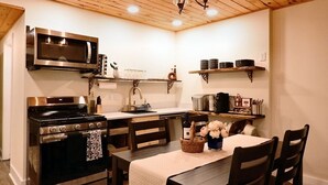 A compact kitchen with a built-in microwave, stove, and oven, wooden ceiling, and a dining area with a table and chairs. - The Aviator: Serene Ambience & Stylish Comfort (Madison)