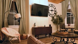 A living room with a flat-screen TV, a wooden coffee table, a cushioned chair, a dark wooden sideboard, and a large wall clock. - The Aviator: Serene Ambience & Stylish Comfort (Madison)