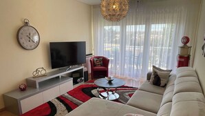 Un salón moderno con un televisor de pantalla plana, un sillón rojo, un sofá color beige y una alfombra estampada.