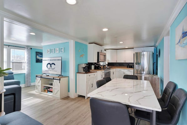 A modern kitchen with white cabinets, a marble dining table, and a seating area with a sofa and chairs.