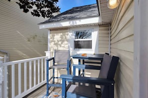 A covered outdoor seating area with a table and chairs, a window, and a white railing.
