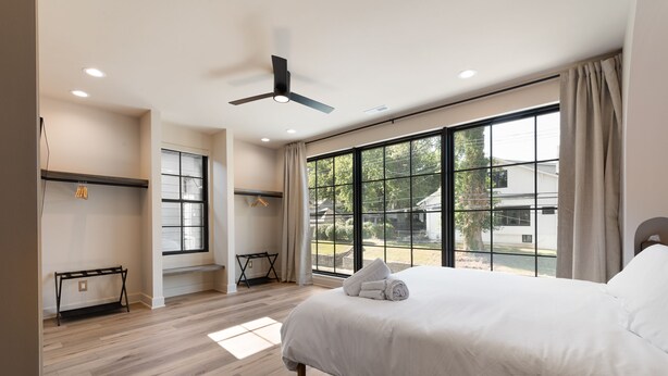 Quarto moderno com uma cama grande, ventoinha no teto, janela com vista para o exterior e chão de madeira.