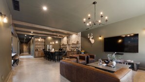 Ampla sala de estar com um sofá de couro marrom, uma mesa de jantar e uma cozinha ao fundo.