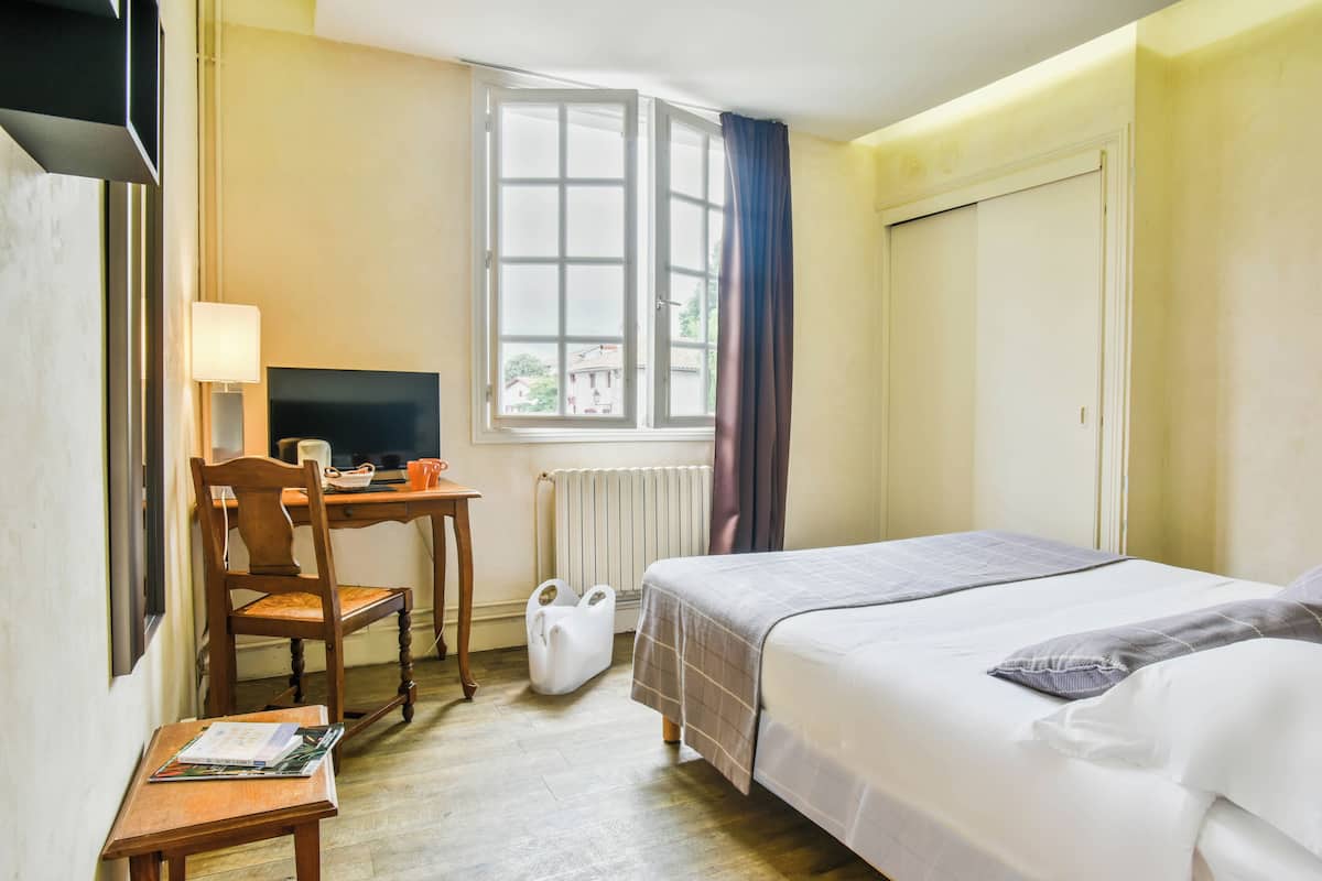 Ein Hotelzimmer mit Bett, Schreibtisch mit Stuhl, Fernseher und einem Fenster mit Vorhängen.