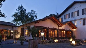 A traditional chalet-style building with a sloped roof and wooden beams, surrounded by a well-lit courtyard with potted plants and a stone pathway. - Hôtel Spa Mendi Alde (Ossès)