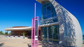 A modern building with a curved facade and a sign for Scarborough Beach Pool. - Coastal Scarborough Beach • Chic • Pool View • 2BR (Scarborough)